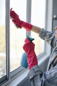 A staff member cleans a window wearing red gloves - and holding a blue spray bottle. 