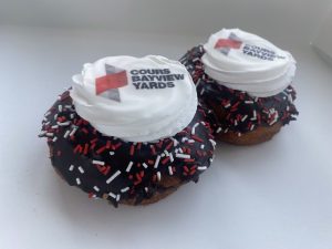 Two chocolate donuts with white frosting have the Bayview Yards logo printed on top of white frosting. 