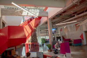 A red, angular metallic staircase winds through an open workspace in Bayview Yards front entrance. 