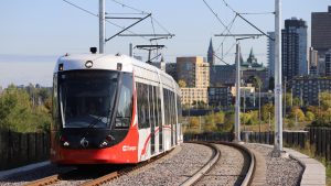 OC Transpo's light rail vehicle on tracks. Ottawa Cityscape in background with views of Parliament of Canada.