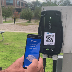 A person uses their phone to interact with an electric vehicle charging unit which displays a QR code.