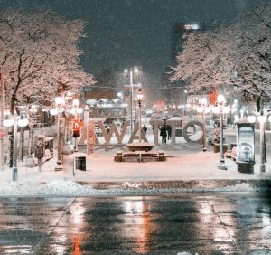 A wintry scene with a view of a sign in the middle of Ottawa's ByWard market that reads 'Ottawa.' The image is from the perspective of behind the sign, so the lettering is backwards. 