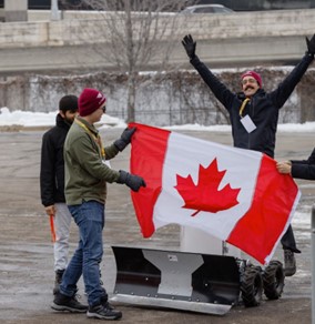 Three people are outside on a cold day with what appears to be an autonomous vehicle. They're holding a Canadian flag and celebrating. 