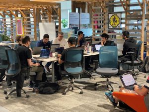 A group is gathered together at a desk, on laptops, working collaboratively. 